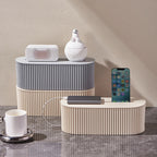 2 boîtes pour câble management de couleur blanc cassé et grise posé sur du sol marbré