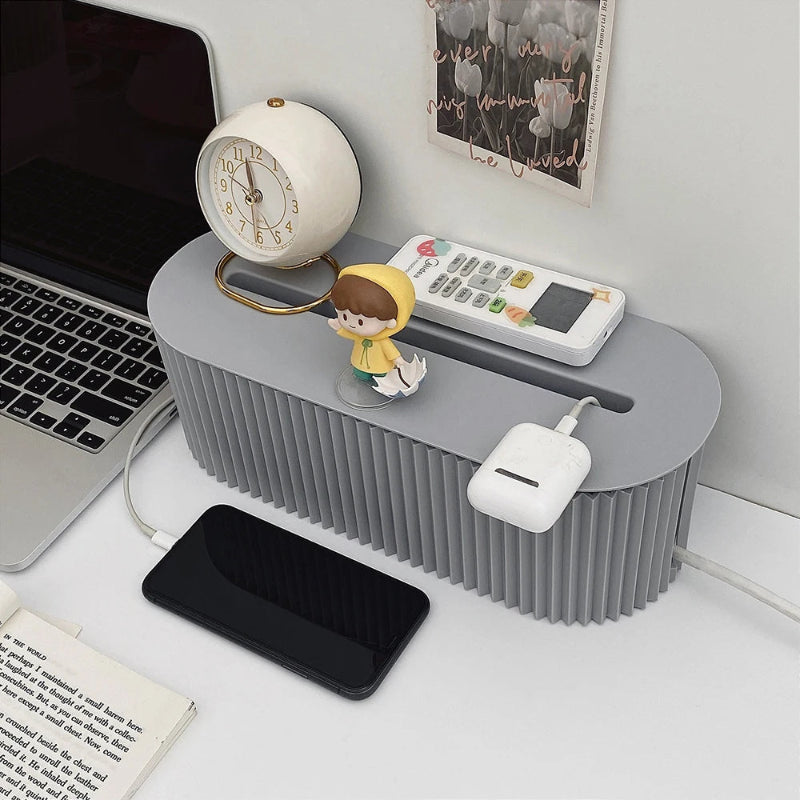 boîte pour câble management de couleur grise avec téléphone et airpods posé sur un bureau