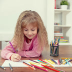 une fille dessine avec porte stylo noir posé sur le sol avec des crayons de couleur à l'intérieur